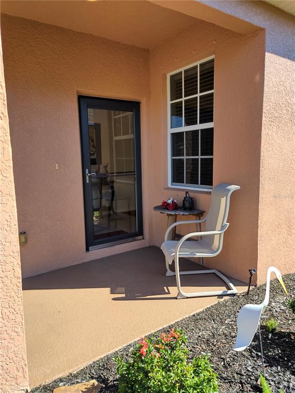 A covered patio features a glass door, a single chair, a small table, and a heron statue — 11997 TEMPEST HARBOR LOOP, VENICE, FL