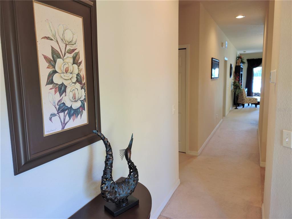 A hallway features a framed floral painting, a decorative sculpture, and carpeted flooring — 11997 TEMPEST HARBOR LOOP, VENICE, FL