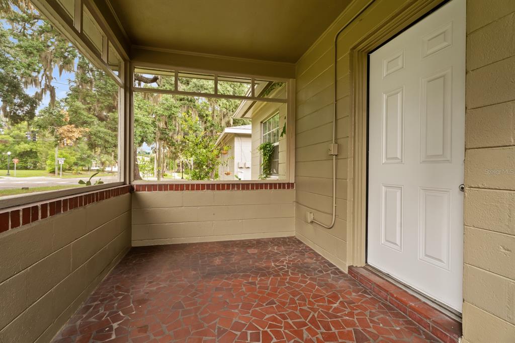 A screened-in porch features a red tiled floor, painted block walls, and a white door — 1008 - 1014 E CENTRAL BOULEVARD, ORLANDO, FL