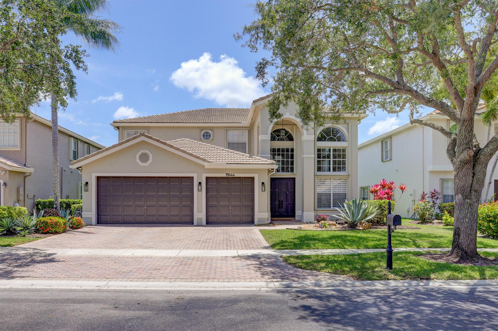 A two-story suburban house features a paved driveway, a three-car garage, and a large tree — 19644 Estuary Drive, Boca Raton FL 33498, BOCA RATON, FL