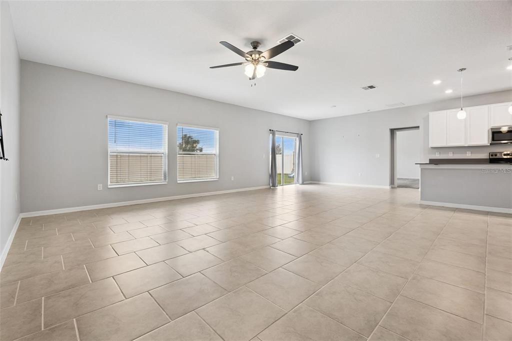 A spacious living area with light-colored tile flooring, a ceiling fan, and an open kitchen — 781 TAURUS LANE, ST CLOUD, FL