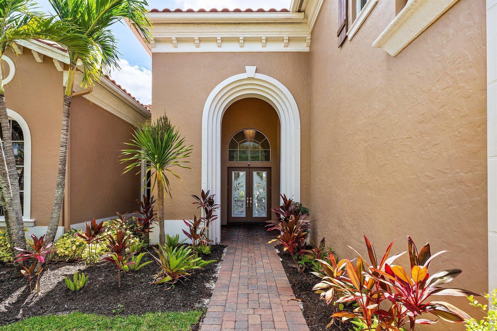 A brick walkway leads to a double front door framed by a white arched entryway — 3381 Lago De Talavera, Lake Worth FL 33467, LAKE WORTH, FL