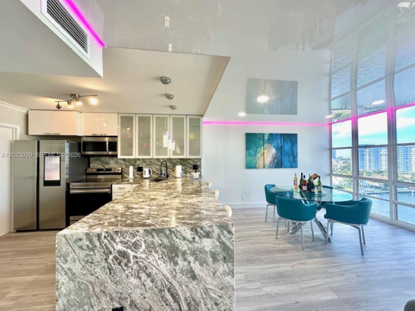 A modern kitchen features a large marble island, white cabinetry, and a glass dining set — 2017 S Ocean Dr # 1107, Hallandale Beach FL 33009, HALLANDALE BEACH, FL