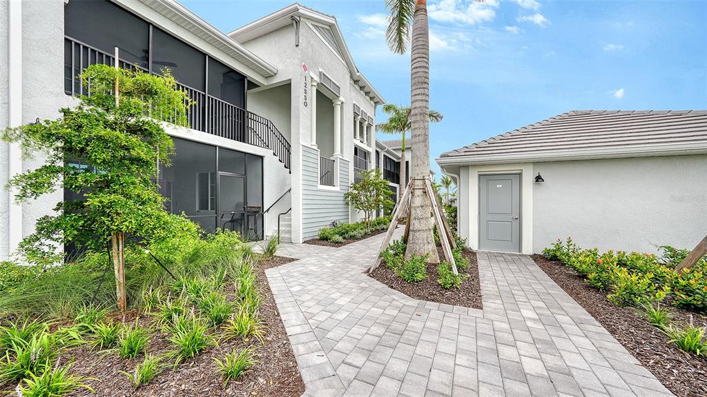 A paved walkway leads to a multi-story building entrance and a separate storage unit — 12550 GALAPAGOS COURT UNIT 206, VENICE, FL