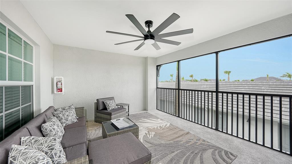A screened-in balcony features gray wicker furniture, a patterned rug, and a ceiling fan — 12550 GALAPAGOS COURT UNIT 206, VENICE, FL