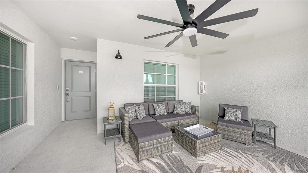 A covered patio features a gray sectional sofa, a matching armchair, and a ceiling fan — 12550 GALAPAGOS COURT UNIT 206, VENICE, FL