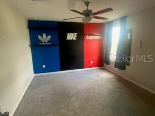 A bedroom features gray carpet, a ceiling fan, and a wall painted with brand logos — 15510 WICKED STRONG STREET, SUN CITY CENTER, FL