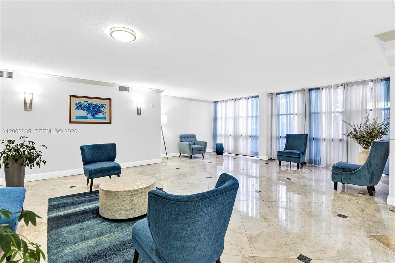 A spacious living room features blue armchairs, a patterned rug, and polished tile flooring — 1000 Parkview Dr # 407, Hallandale Beach FL 33009, HALLANDALE BEACH, FL