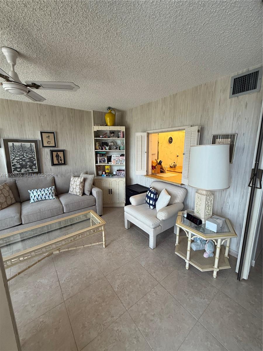 A living room features a gray sofa, striped armchair, glass coffee table, and wood-paneled walls — 1000 Parkview Dr # 407, Hallandale Beach FL 33009, HALLANDALE BEACH, FL