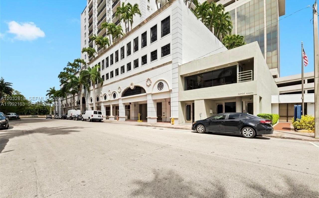 A multi-story building with a parking garage, palm trees, and a parked black sedan — 357 Almeria Ave # 802, Coral Gables FL 33134, CORAL GABLES, FL
