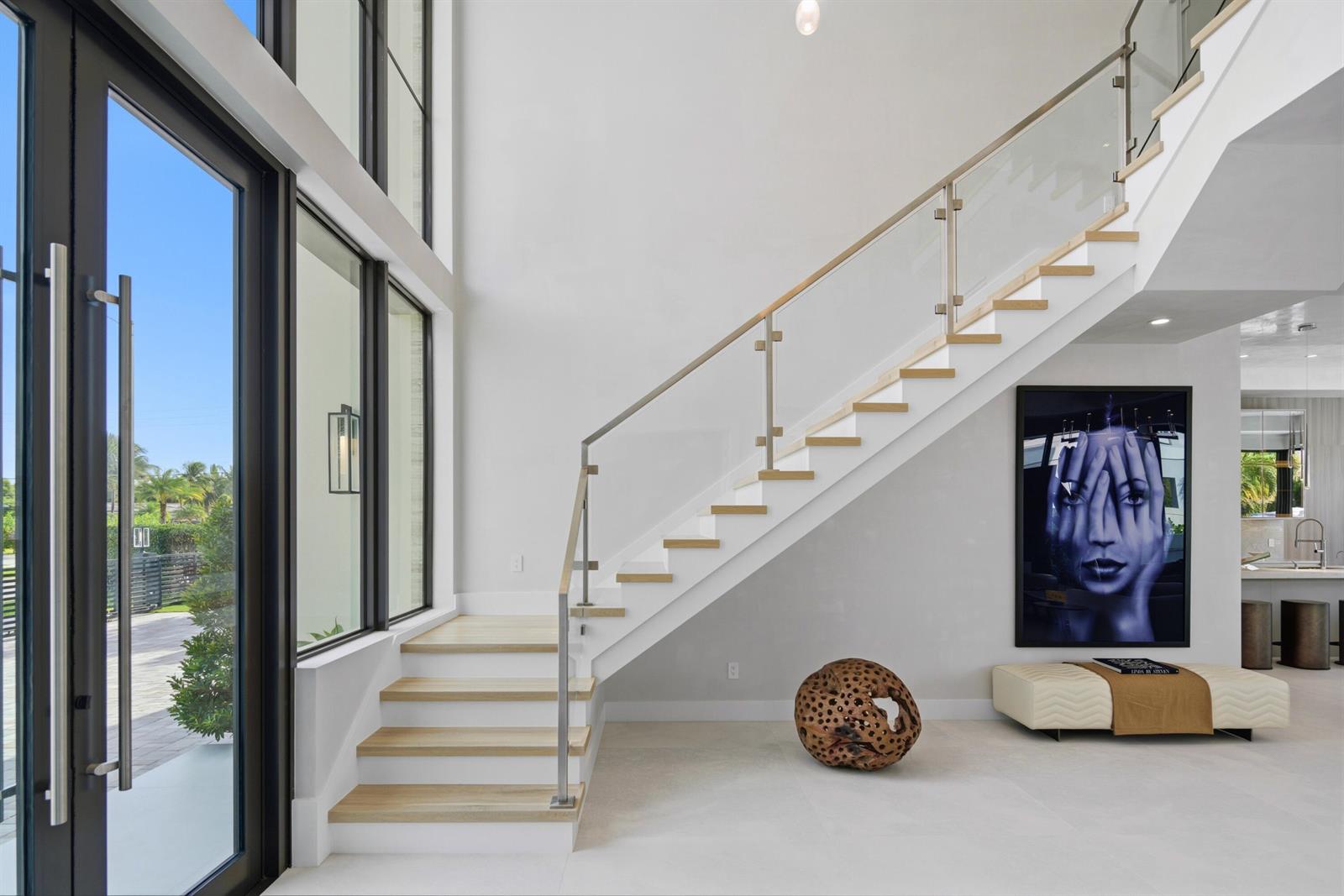 A modern entryway features a floating staircase with glass railings, light wood treads, and artwork — 511 Silver Lane, Boca Raton FL 33432, BOCA RATON, FL