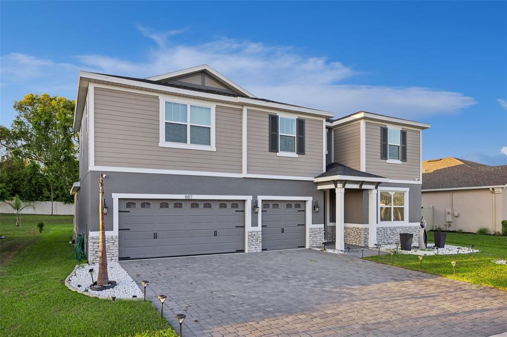A two-story house features a three-car garage, stone accents, and a paved driveway — 887 ASTERFIELD LANE, DELAND, FL