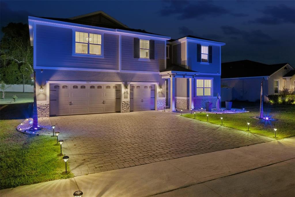 A two-story house with a paved driveway, garage, and landscape lighting at night — 887 ASTERFIELD LANE, DELAND, FL