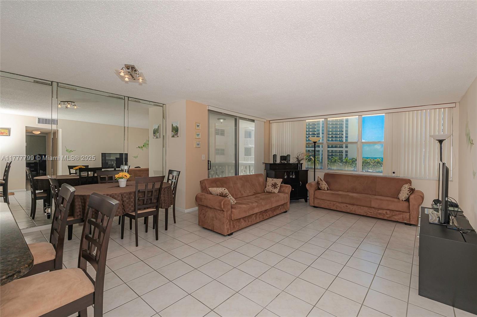 A living and dining area features tile flooring, mirrored walls, and two brown sofas — 1817 S Ocean Dr # 628, Hallandale Beach FL 33009, HALLANDALE BEACH, FL