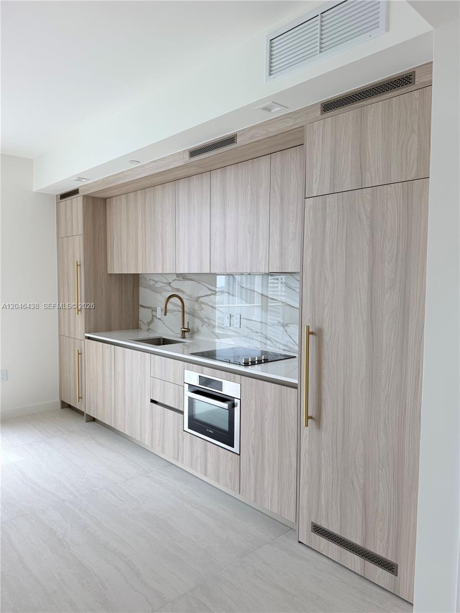 A modern kitchen features light wood cabinetry, a marble backsplash, and integrated stainless steel appliances — 77 SE 5th Street # 1915, Miami FL 33131, MIAMI, FL