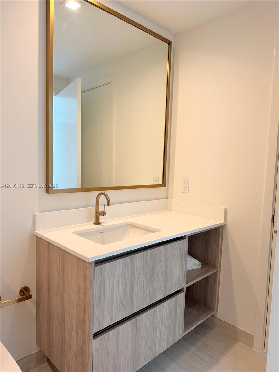 A modern bathroom features a wood-grain vanity, white countertop, gold faucet, and a large mirror — 77 SE 5th Street # 1915, Miami FL 33131, MIAMI, FL