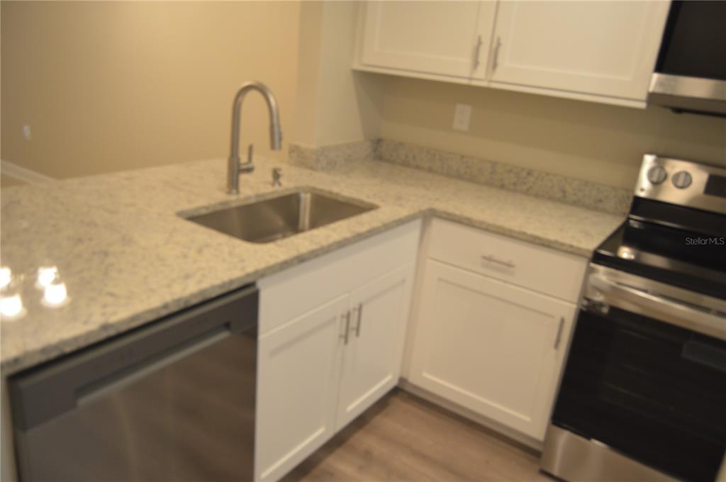 A kitchen features white cabinets, speckled countertops, a stainless steel sink, and stainless steel appliances — 2849 STILLWELL COURT, NEW PORT RICHEY, FL
