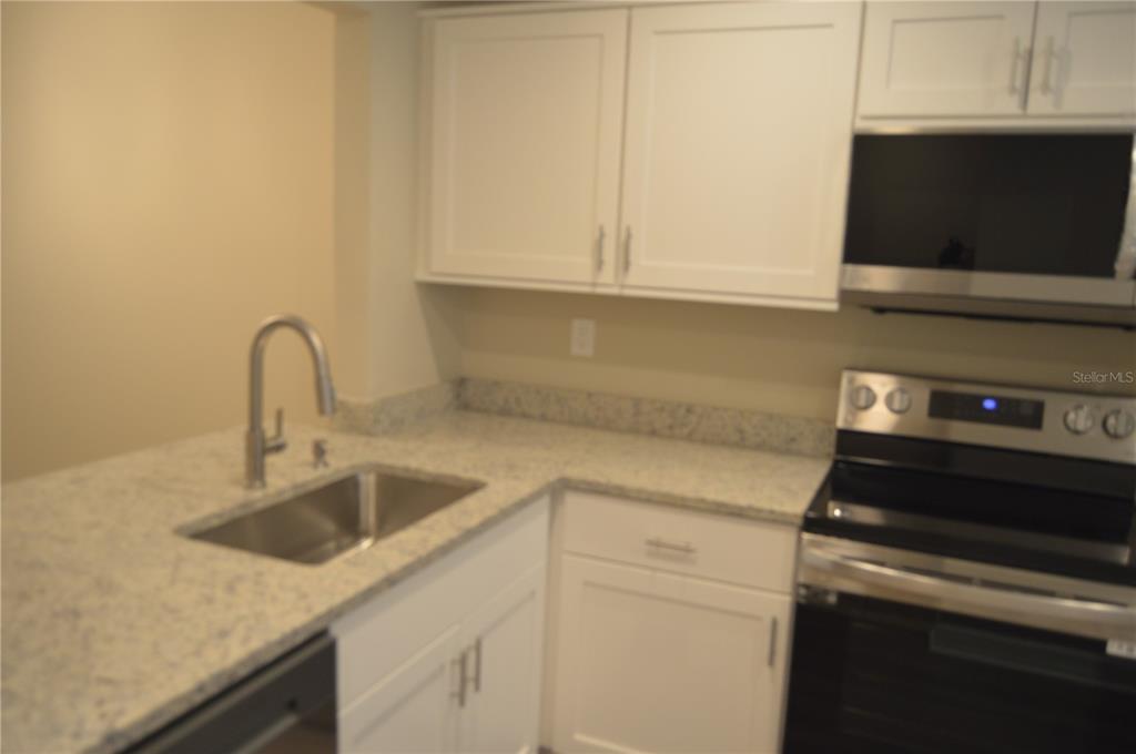 A kitchen features white cabinets, granite countertops, a stainless steel sink, and stainless steel appliances — 2849 STILLWELL COURT, NEW PORT RICHEY, FL