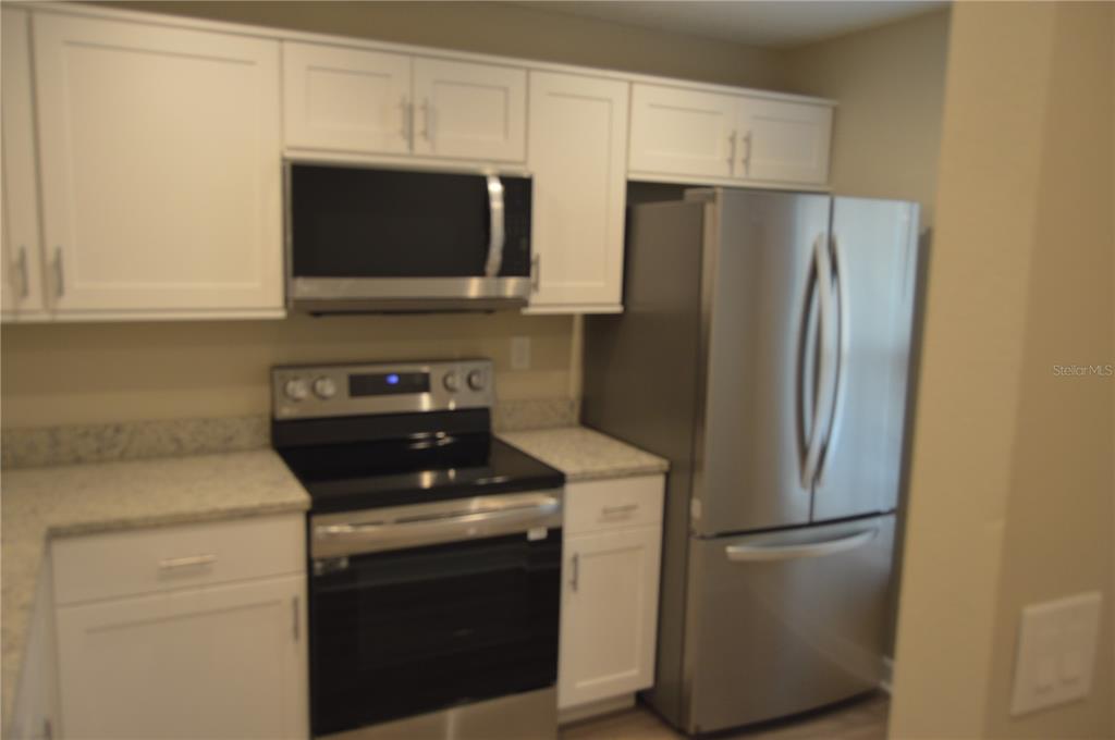 A kitchen features white cabinets, stainless steel appliances, and light-colored granite countertops — 2849 STILLWELL COURT, NEW PORT RICHEY, FL