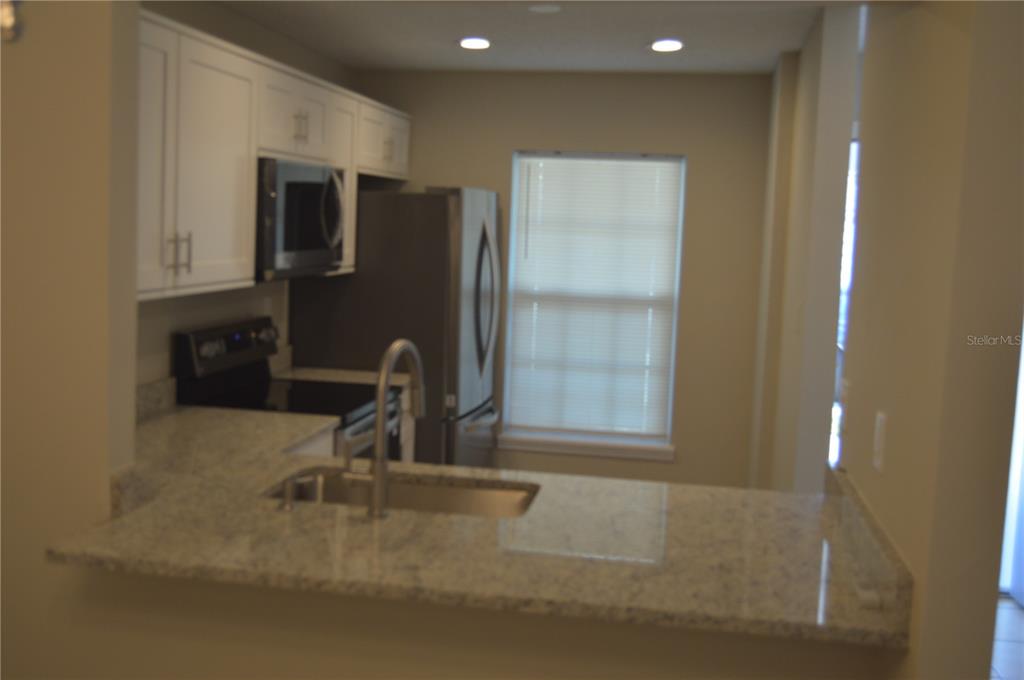 A kitchen features white cabinets, granite countertops, stainless steel appliances, and a breakfast bar — 2849 STILLWELL COURT, NEW PORT RICHEY, FL
