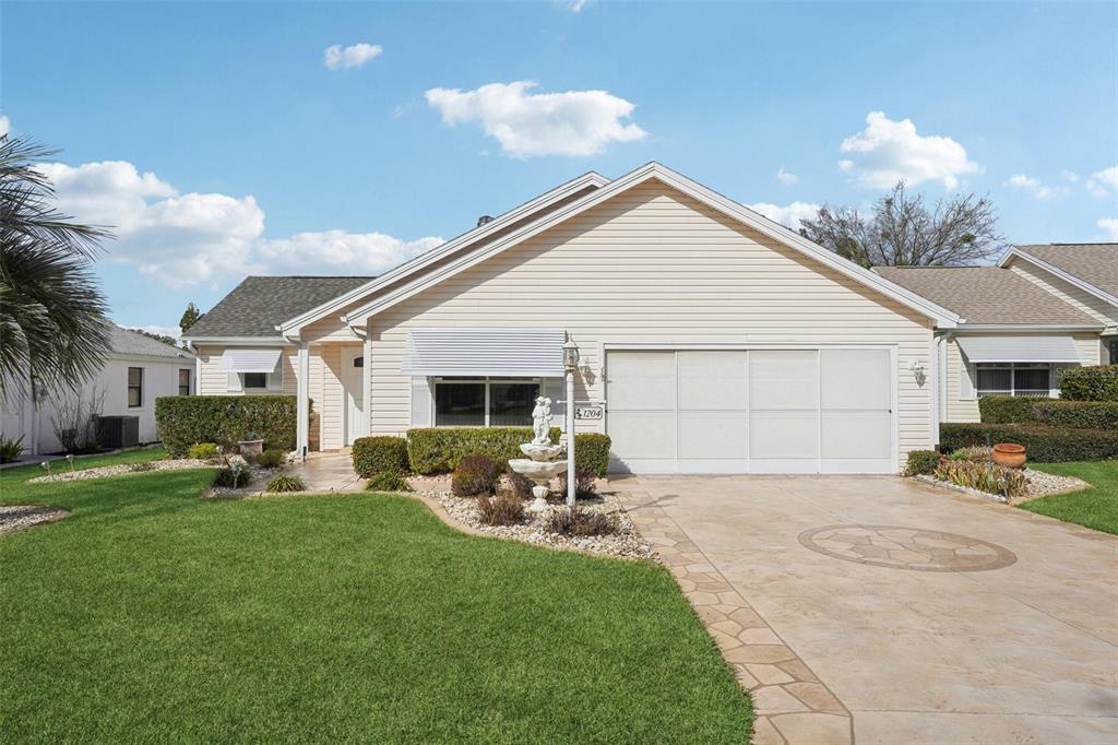 A single-story house with beige siding, a garage, and a front lawn with a fountain — 1204 BARCELONA DRIVE, THE VILLAGES, FL