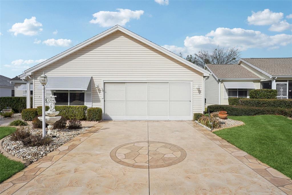 A single-story house with a beige garage door, a decorative driveway, and a front fountain — 1204 BARCELONA DRIVE, THE VILLAGES, FL