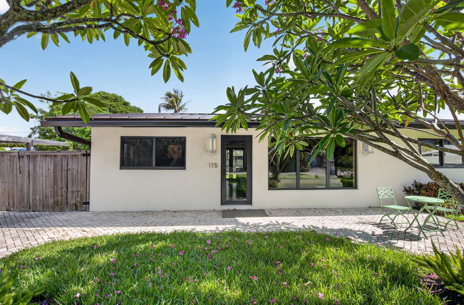 A single-story house exterior with a paved patio, green lawn, and a large flowering tree — 115 NW 7th Street, Boca Raton FL 33432, BOCA RATON, FL