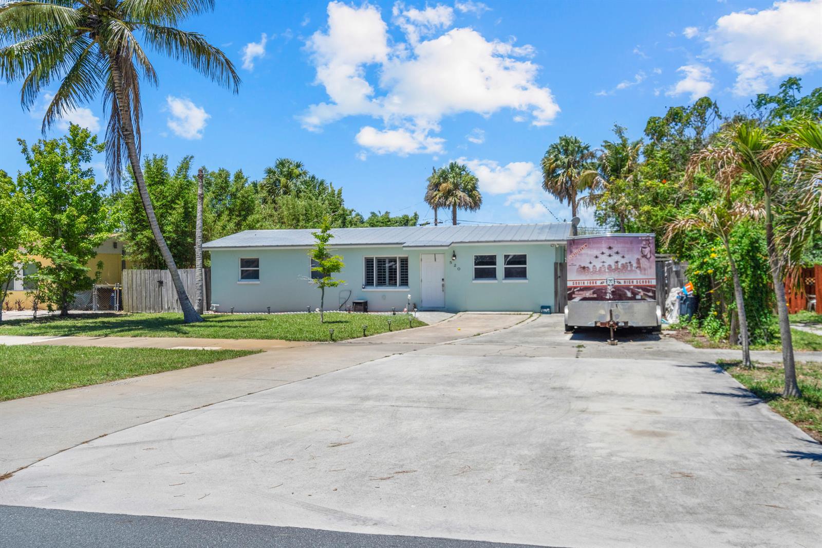 A light green single-story house with a metal roof sits behind a large concrete driveway — 520 SE Dolphin Drive, Stuart FL 34996, STUART, FL