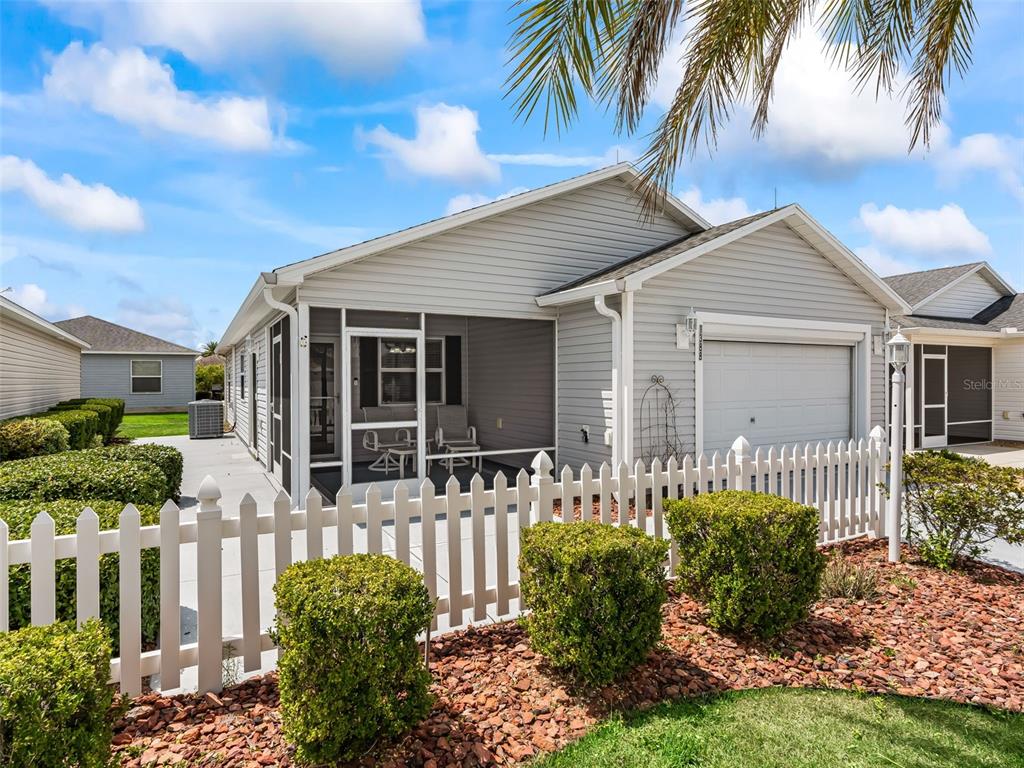 A light gray house with a screened-in porch, white picket fence, and a garage — 1388 VIOLA COURT, THE VILLAGES, FL