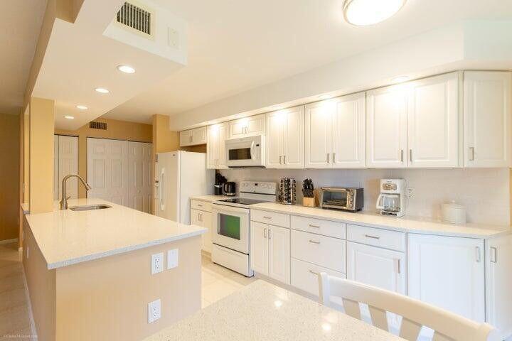 A kitchen features white cabinets, light countertops, stainless steel appliances, and a breakfast bar — 110 Half Moon Circle # E2, Hypoluxo FL 33462, HYPOLUXO, FL