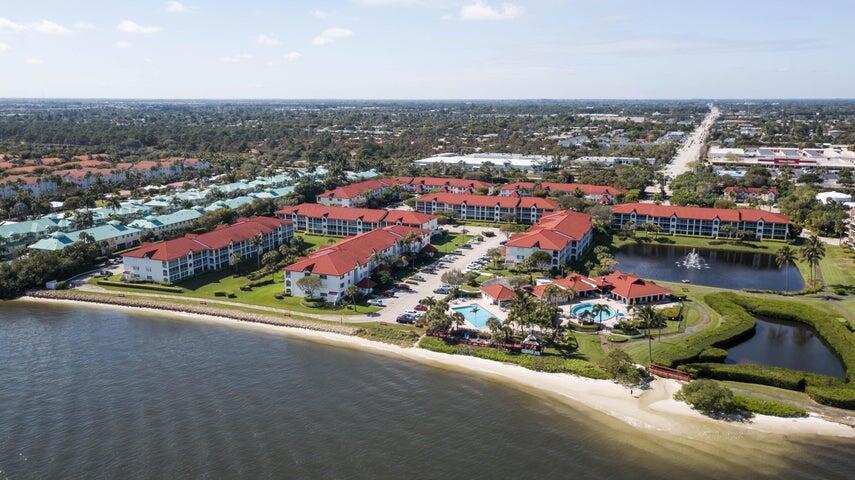 Aerial view of a waterfront apartment complex with red roofs, swimming pools, and a pond — 110 Half Moon Circle # E2, Hypoluxo FL 33462, HYPOLUXO, FL