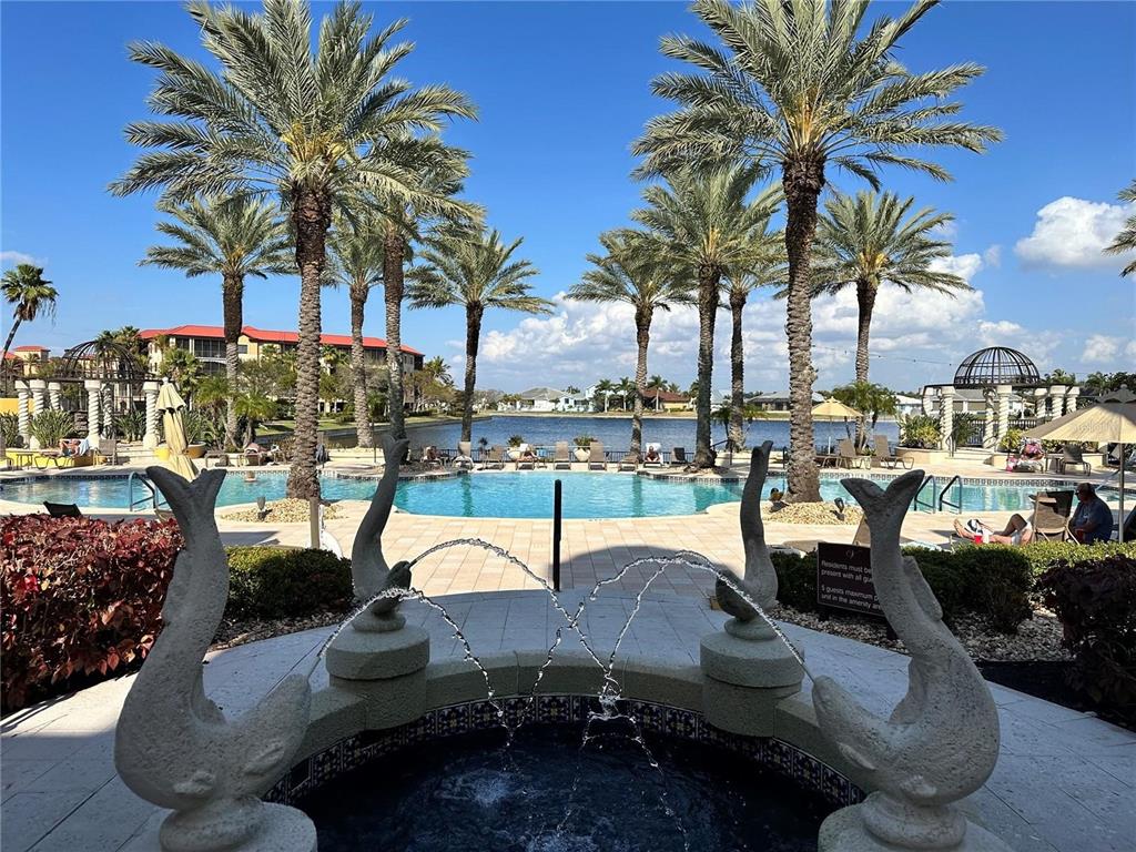 A stone fountain with dolphin sculptures sits in the foreground of a resort-style swimming pool — 98 VIVANTE BOULEVARD UNIT 98315, PUNTA GORDA, FL