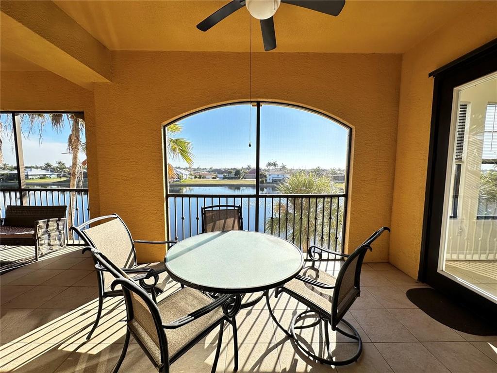 A covered patio features a glass-top table, chairs, and a view of a lake — 98 VIVANTE BOULEVARD UNIT 98315, PUNTA GORDA, FL
