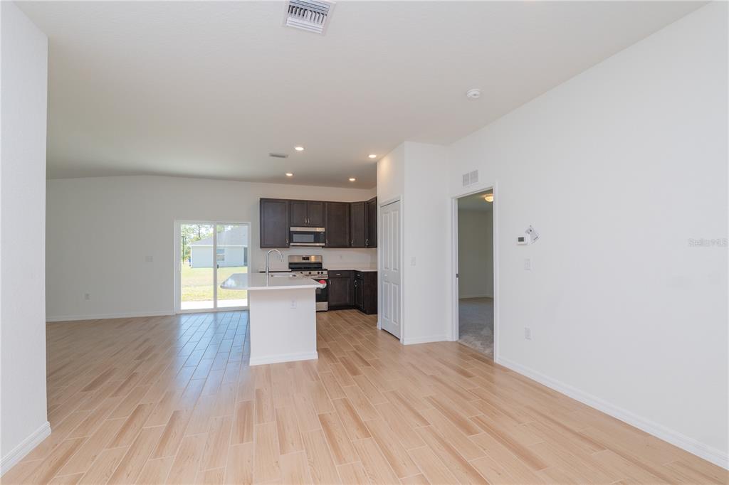 An open-concept kitchen and living area features light wood-look tile flooring and dark cabinetry — 4569 SAN LORENZO DRIVE, SEBRING, FL
