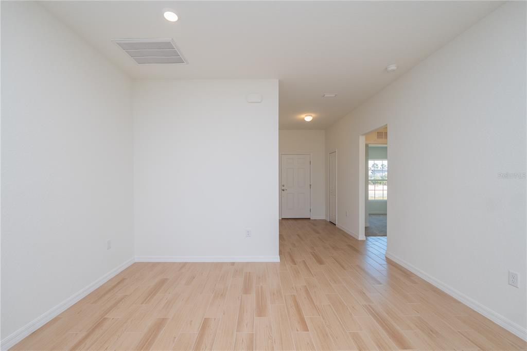 An empty room with light wood-look tile flooring, white walls, and a doorway leading outside — 4569 SAN LORENZO DRIVE, SEBRING, FL
