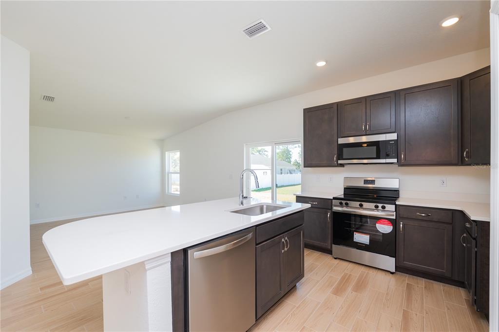 A modern kitchen features dark wood cabinets, stainless steel appliances, and a white quartz island — 4569 SAN LORENZO DRIVE, SEBRING, FL
