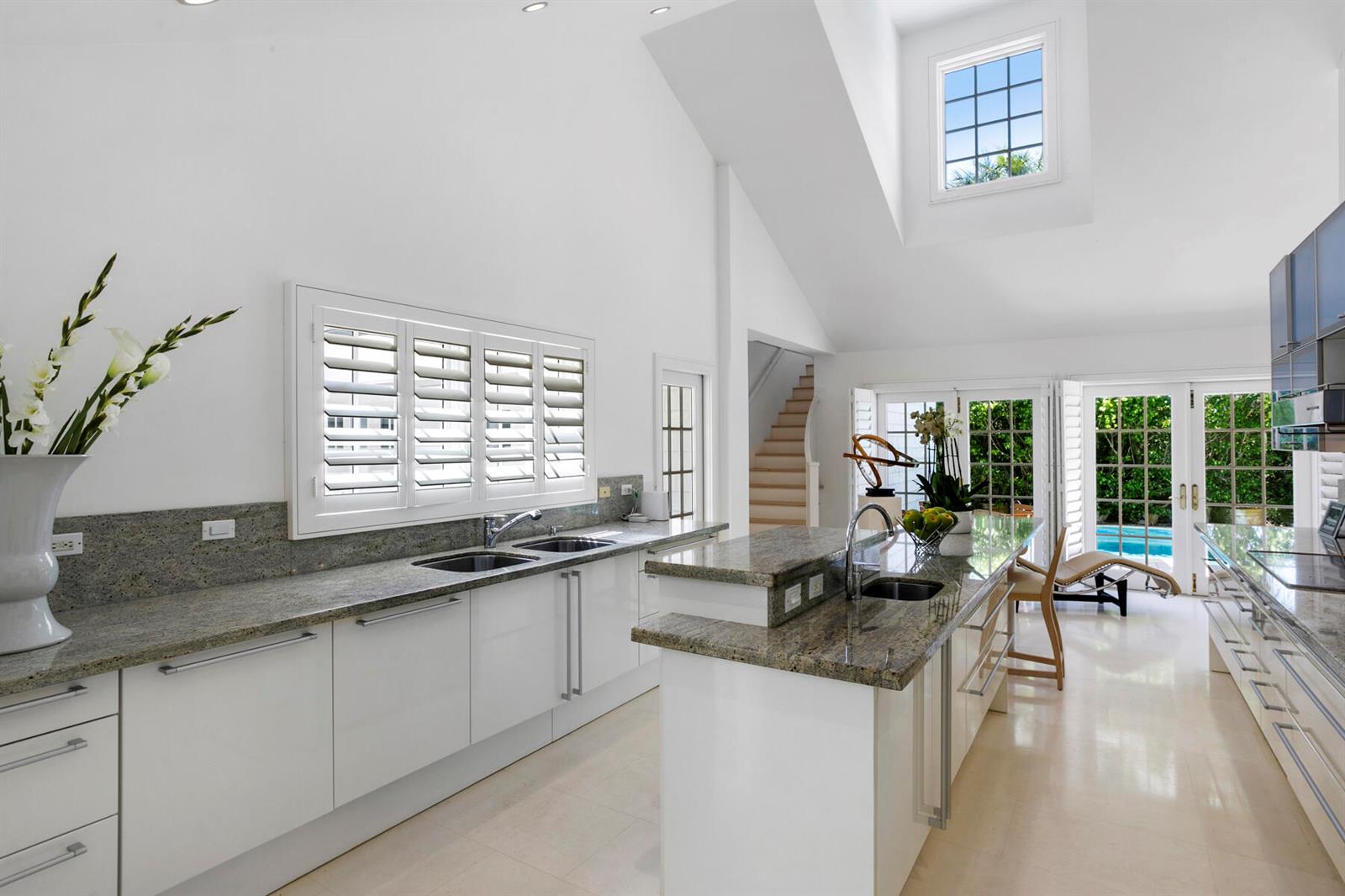 A bright, modern kitchen features white cabinetry, granite countertops, and a view of a pool — 222 Monterey Road, Palm Beach FL 33480, PALM BEACH, FL