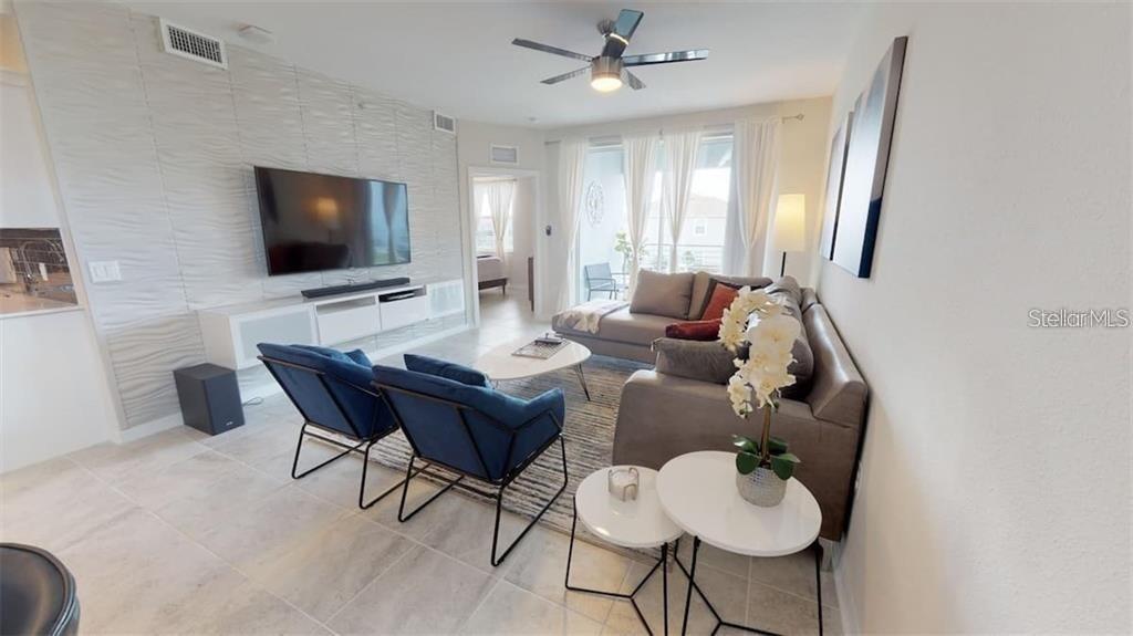 A modern living room features a textured accent wall, blue armchairs, and a gray sofa — 3111 PARADOX CIRCLE UNIT 208, KISSIMMEE, FL