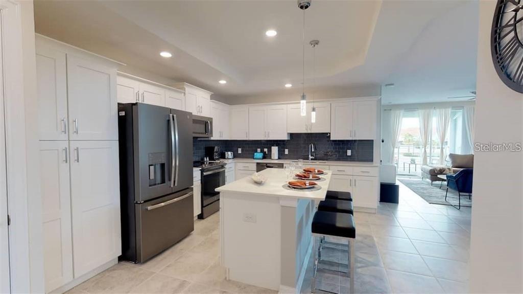 A modern kitchen features white cabinetry, a large island with bar seating, and stainless appliances — 3111 PARADOX CIRCLE UNIT 208, KISSIMMEE, FL