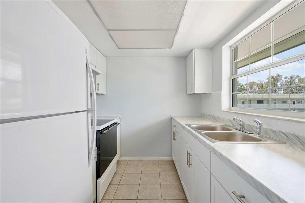 A galley-style kitchen features white cabinets, a white refrigerator, a stove, and marble-look countertops — 1433 S BELCHER ROAD UNIT G16, CLEARWATER, FL