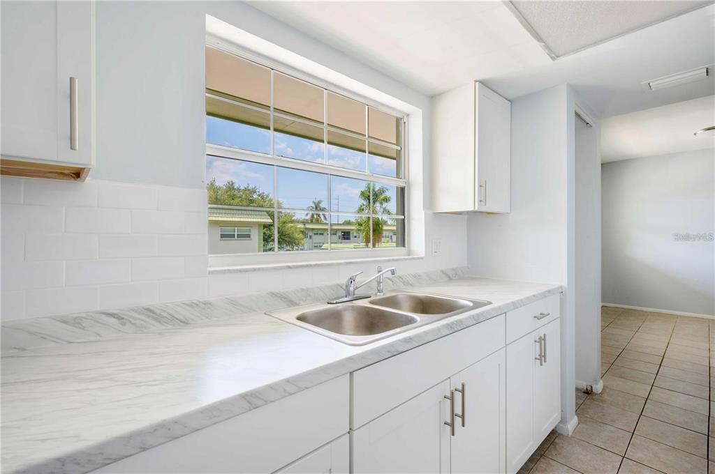 A kitchen with white cabinets, marble-look countertops, a double sink, and a window view — 1433 S BELCHER ROAD UNIT G16, CLEARWATER, FL