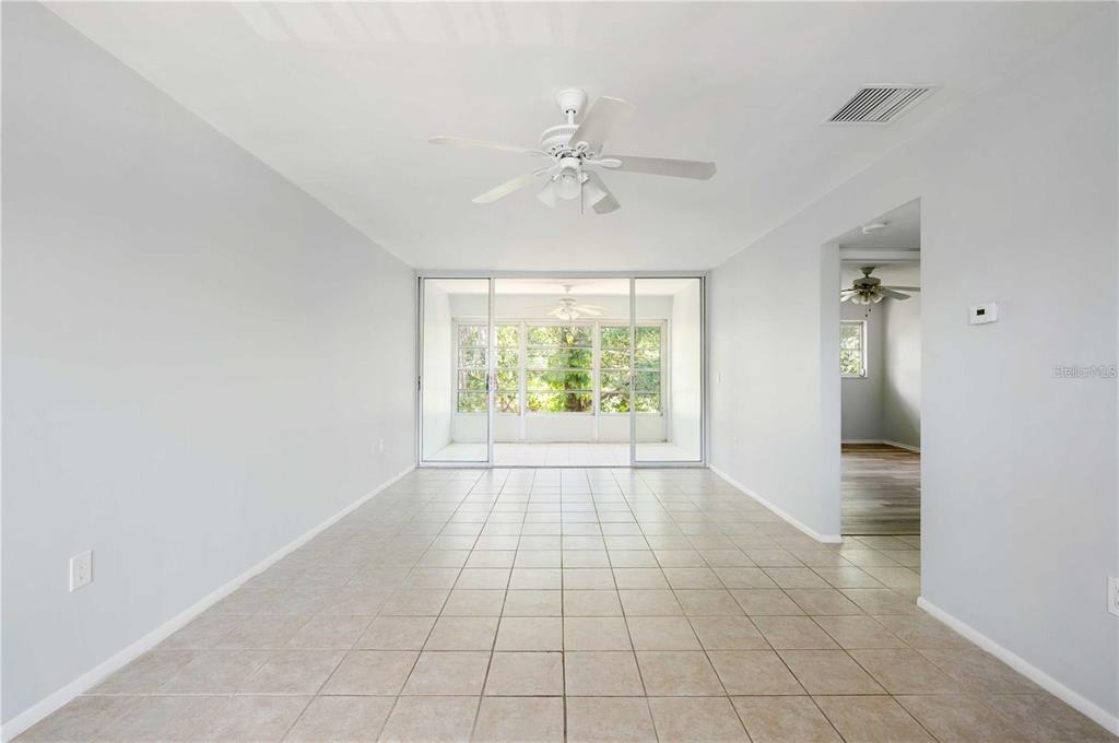 A bright, empty room with light-colored tile flooring, a ceiling fan, and sliding glass doors — 1433 S BELCHER ROAD UNIT G16, CLEARWATER, FL