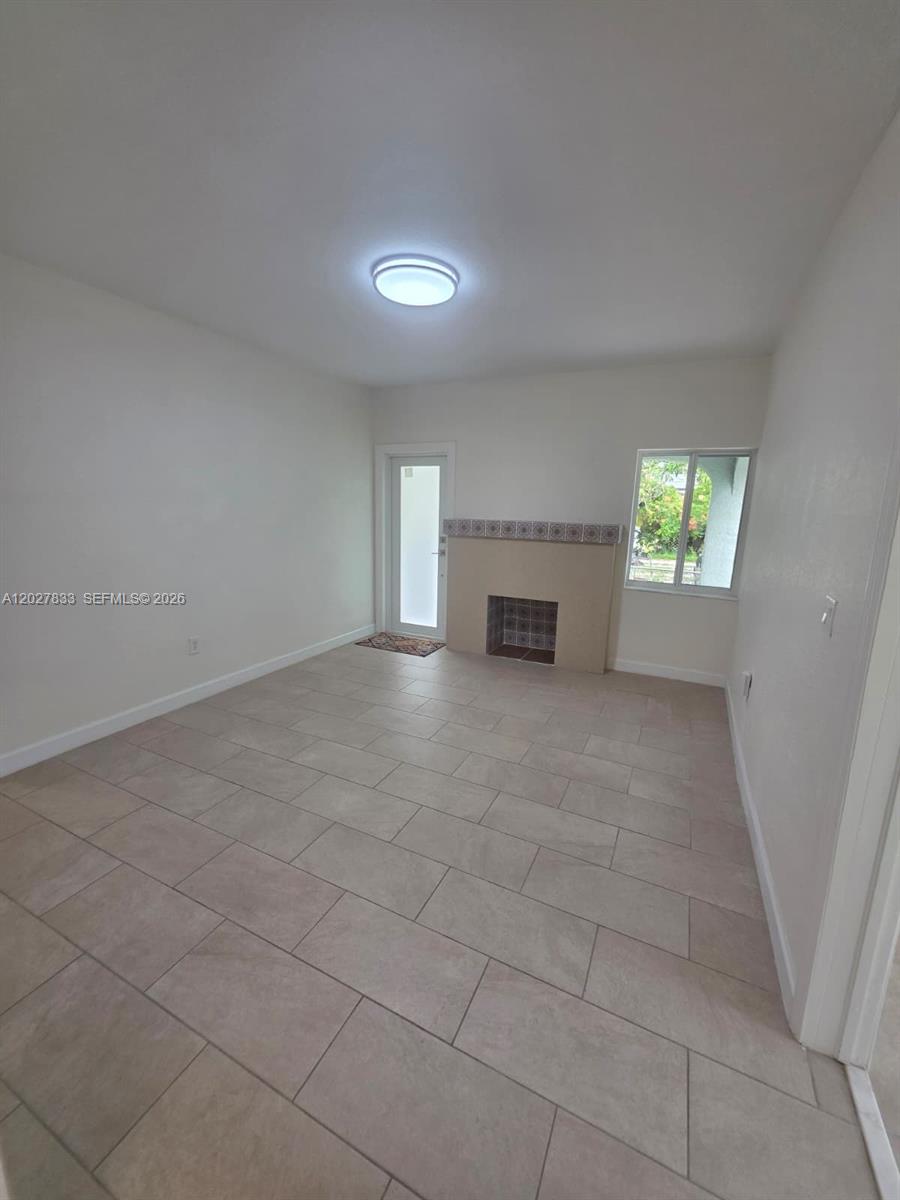 A room with light-colored tile flooring, a fireplace, a window, and a glass-paneled door — 1139 NW 37th St, Miami FL 33127, MIAMI, FL