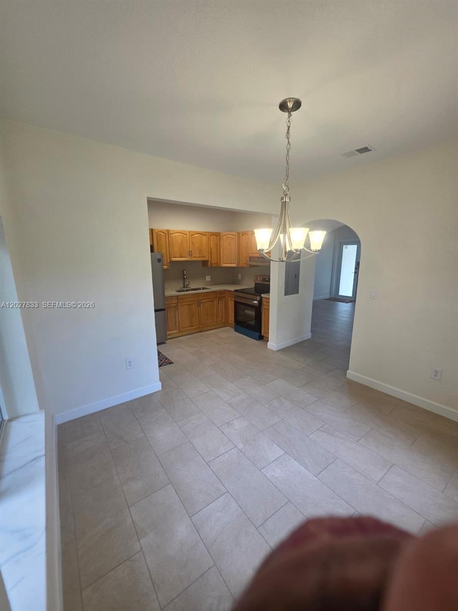 A kitchen with light wood cabinets and tile flooring opens into a dining area — 1139 NW 37th St, Miami FL 33127, MIAMI, FL