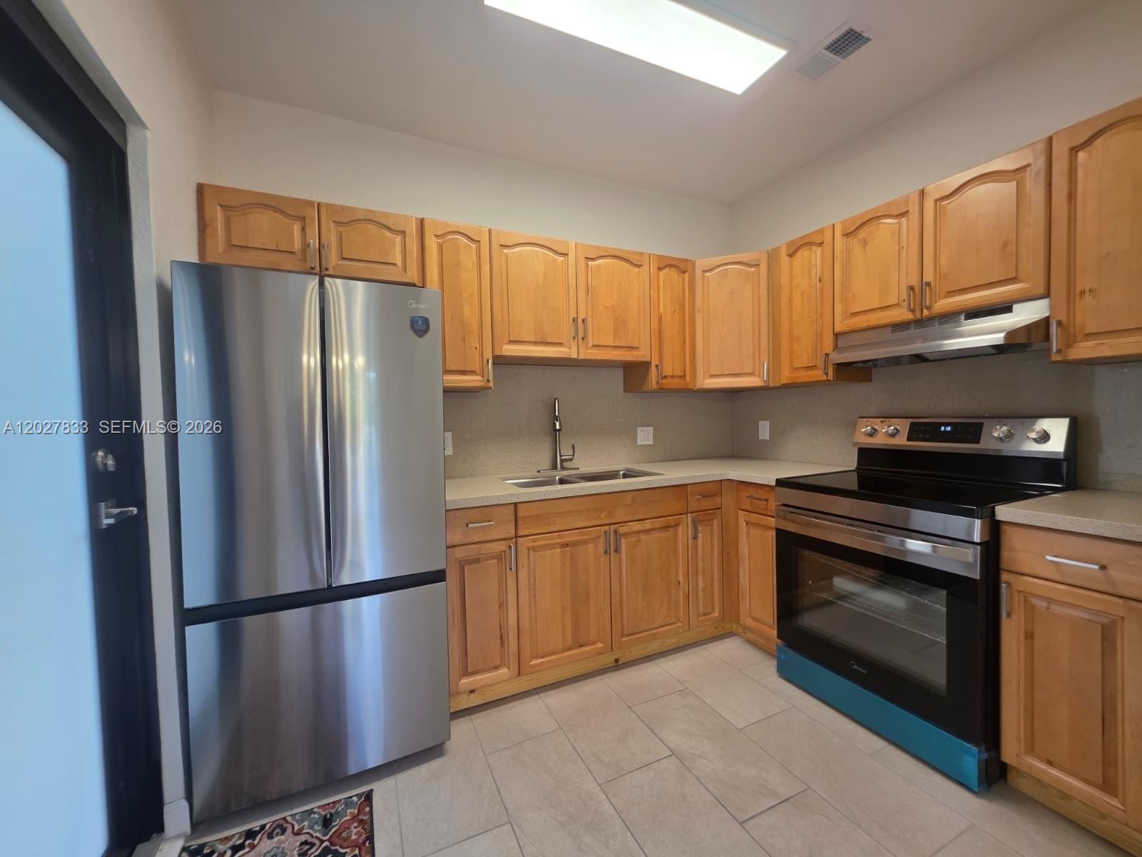 A kitchen features light wood cabinets, stainless steel appliances, and light-colored tile flooring — 1139 NW 37th St, Miami FL 33127, MIAMI, FL