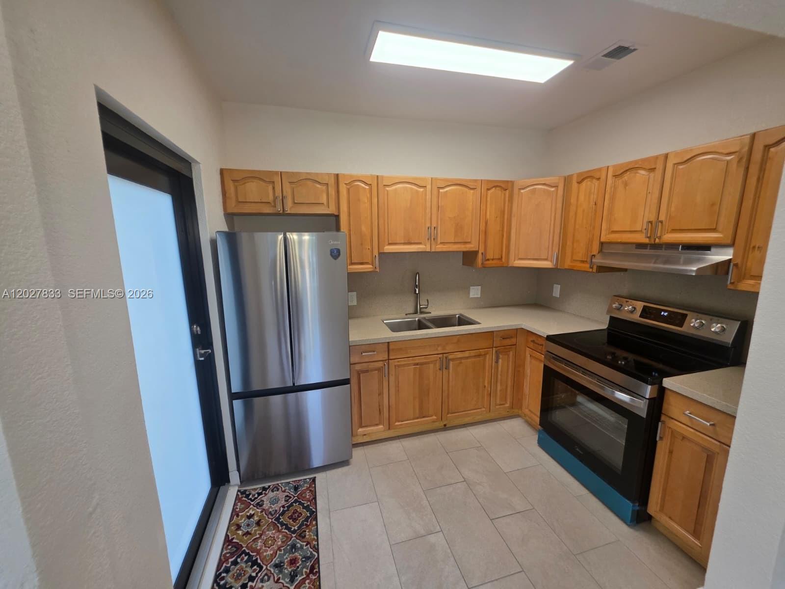 A kitchen features wooden cabinets, stainless steel appliances, light countertops, and gray tile flooring — 1139 NW 37th St, Miami FL 33127, MIAMI, FL