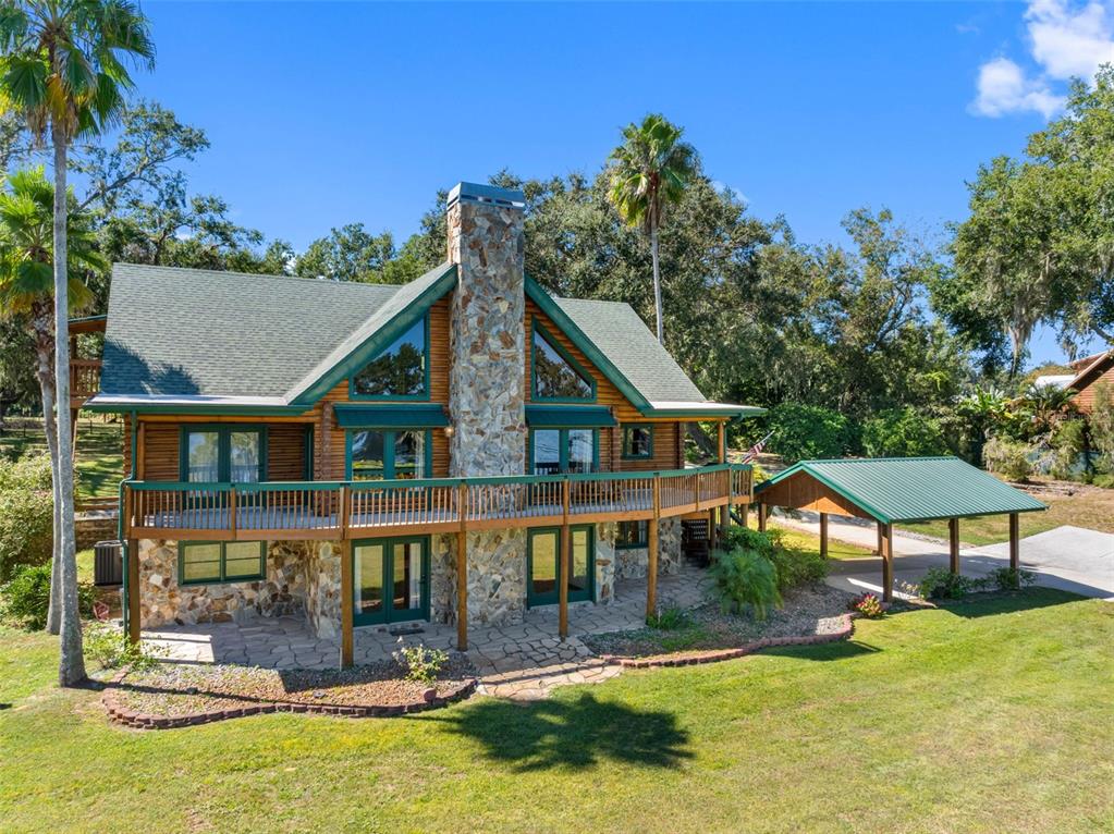 A two-story log cabin with a stone chimney, wrap-around deck, and a detached metal carport — 11401 THONOTOSASSA ROAD, THONOTOSASSA, FL