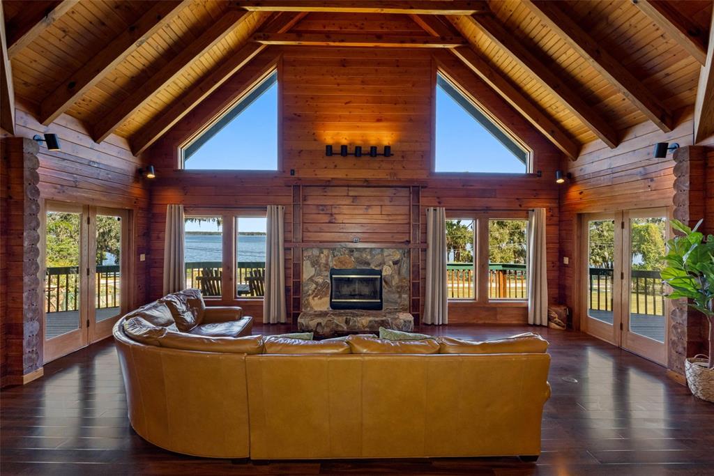 A spacious log cabin living room with a stone fireplace, vaulted ceiling, and lake views — 11401 THONOTOSASSA ROAD, THONOTOSASSA, FL