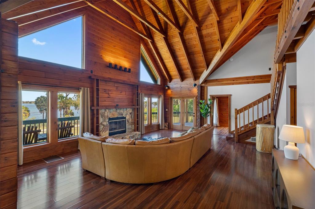 A spacious living room features wood walls, vaulted ceilings, a stone fireplace, and lake views — 11401 THONOTOSASSA ROAD, THONOTOSASSA, FL