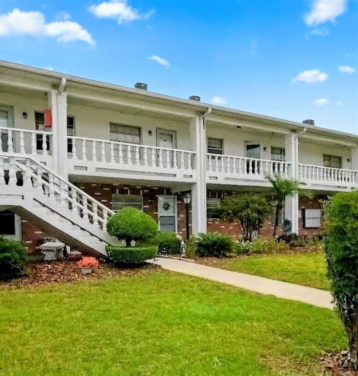 A two-story apartment building features white railings, exterior staircases, and brick accents on the lower level — 4744 AZALEA DRIVE UNIT 204, NEW PORT RICHEY, FL